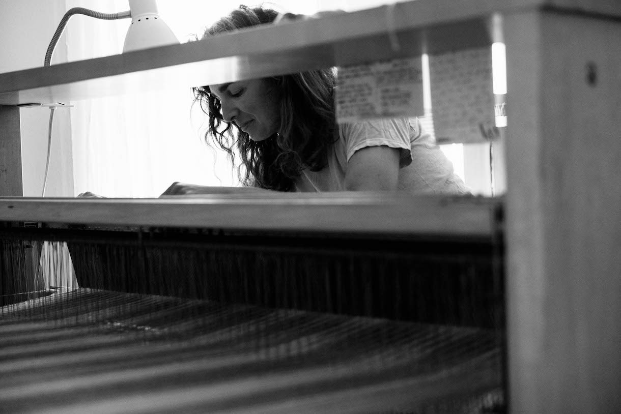 A black and white photo of a woman weaving on a loom.